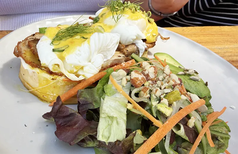 A plate of eggs benedict with a side salad on a wooden table at Tótem restaurant in Centro Histórico, Mazatlán.