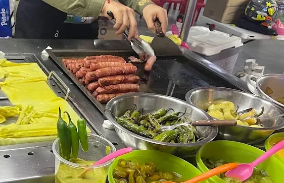 Bacon-wrapped hot dogs sizzling on a flat top grill alongside warming buns at Hot Dogs El Charly in Mazatlán.