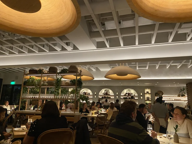Khâluna dining room with large pendant lights, wood furnishings and a bar in the background.