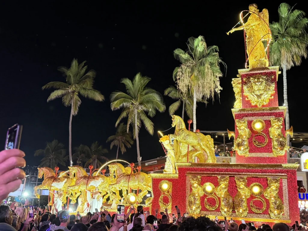 Illuminated red and gold Carnaval float passing palm trees at night in Mazatlán.