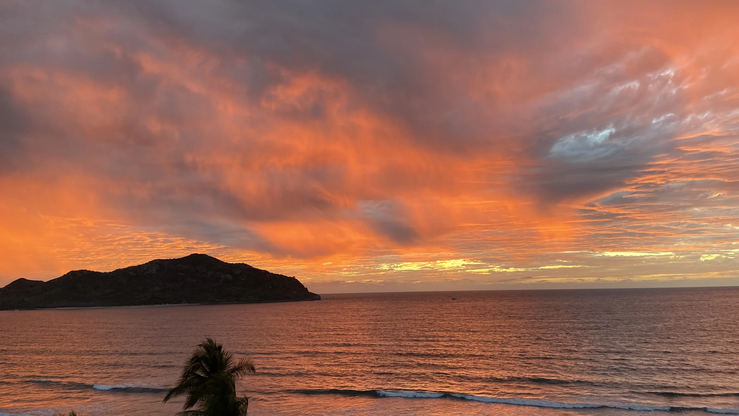 Orange and pink sunset over the Pacific with a silhouetted island and palms in Mazatlán.